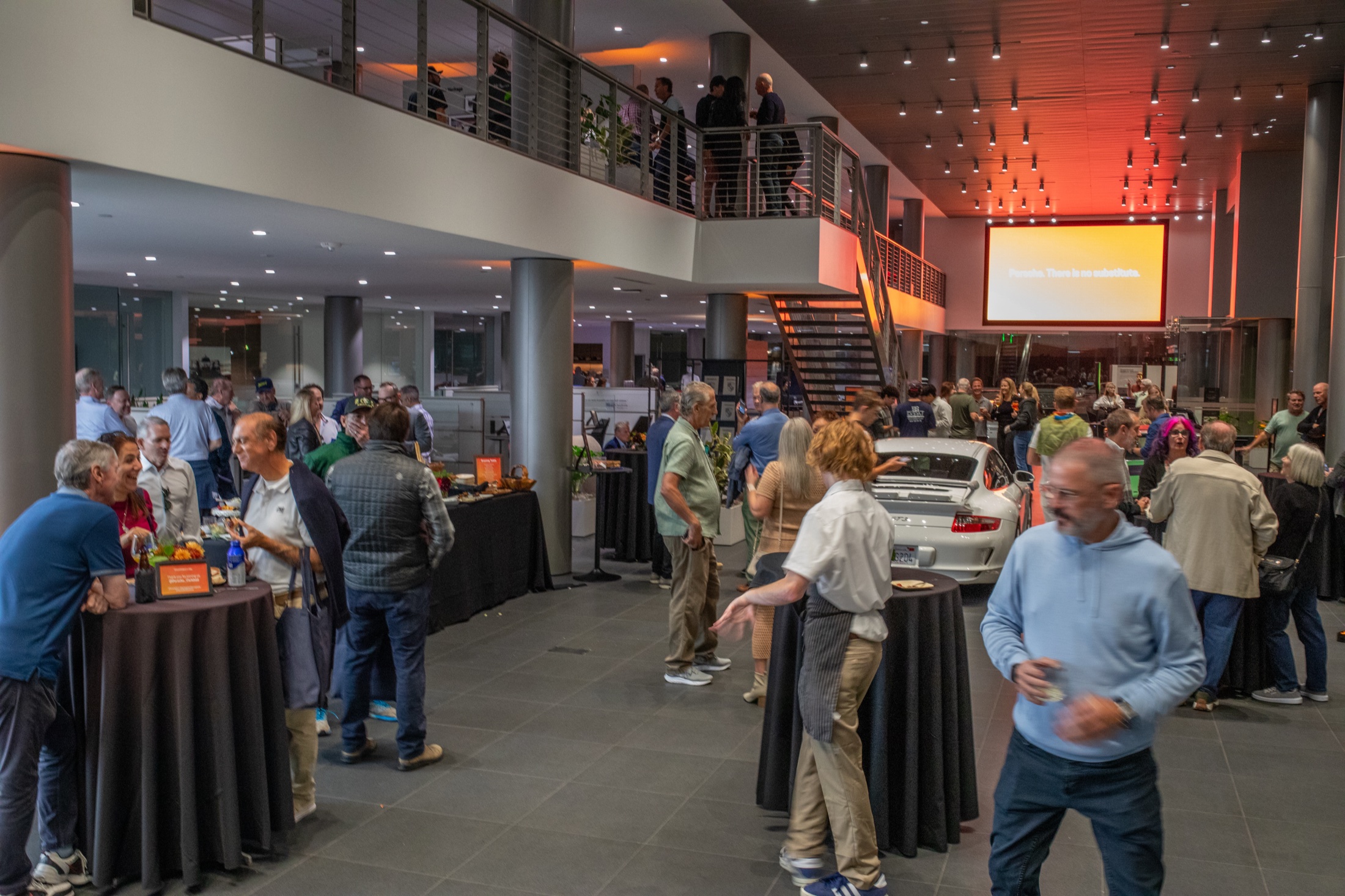 Guests mingling in the warmly lit Porsche Carlsbad showroom during the 911 Heritage and Horsepower evening