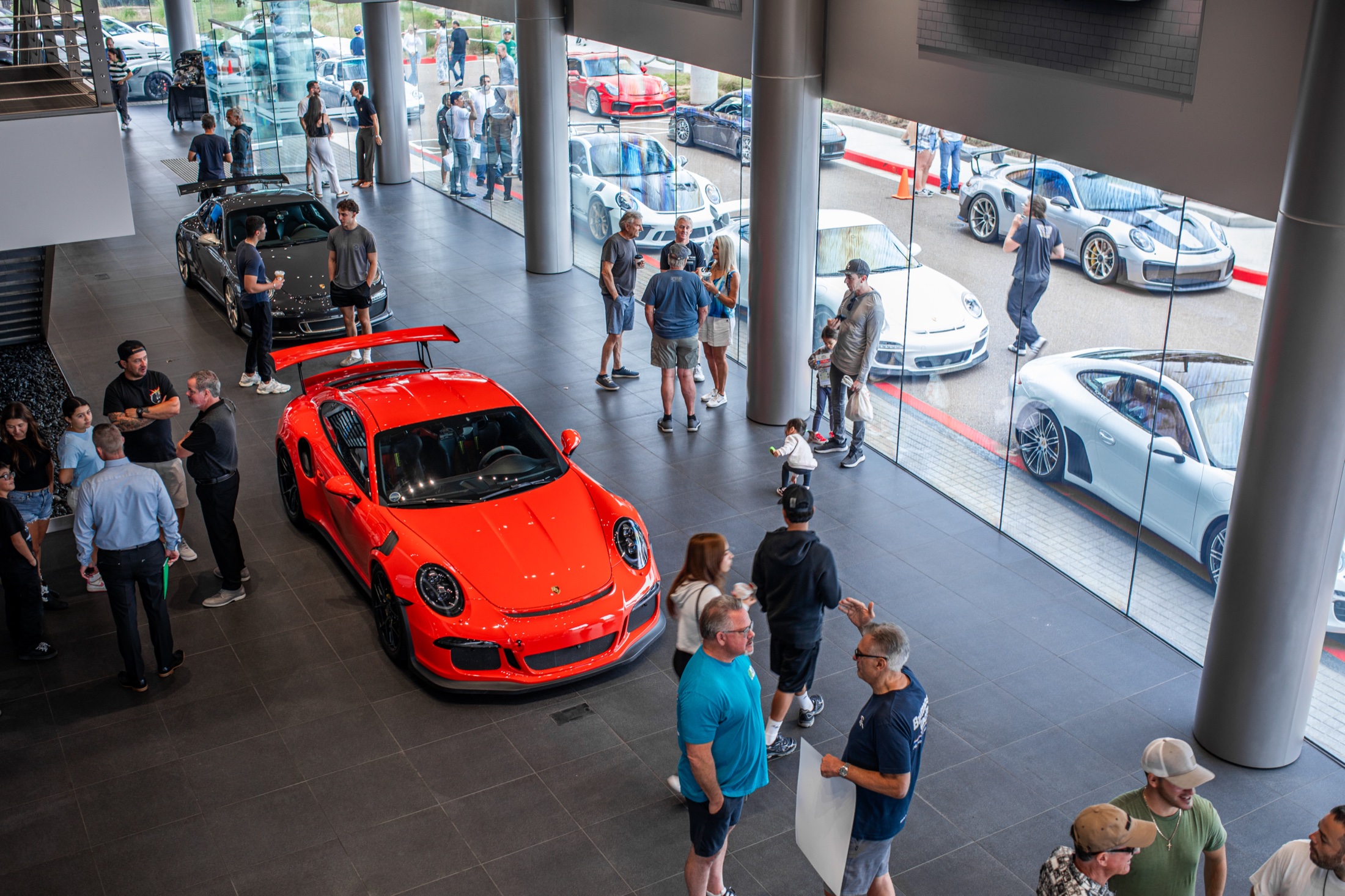 Crowd around an orange 911 GT3 in the Porsche Carlsbad showroom during the anniversary Cars and Coffee