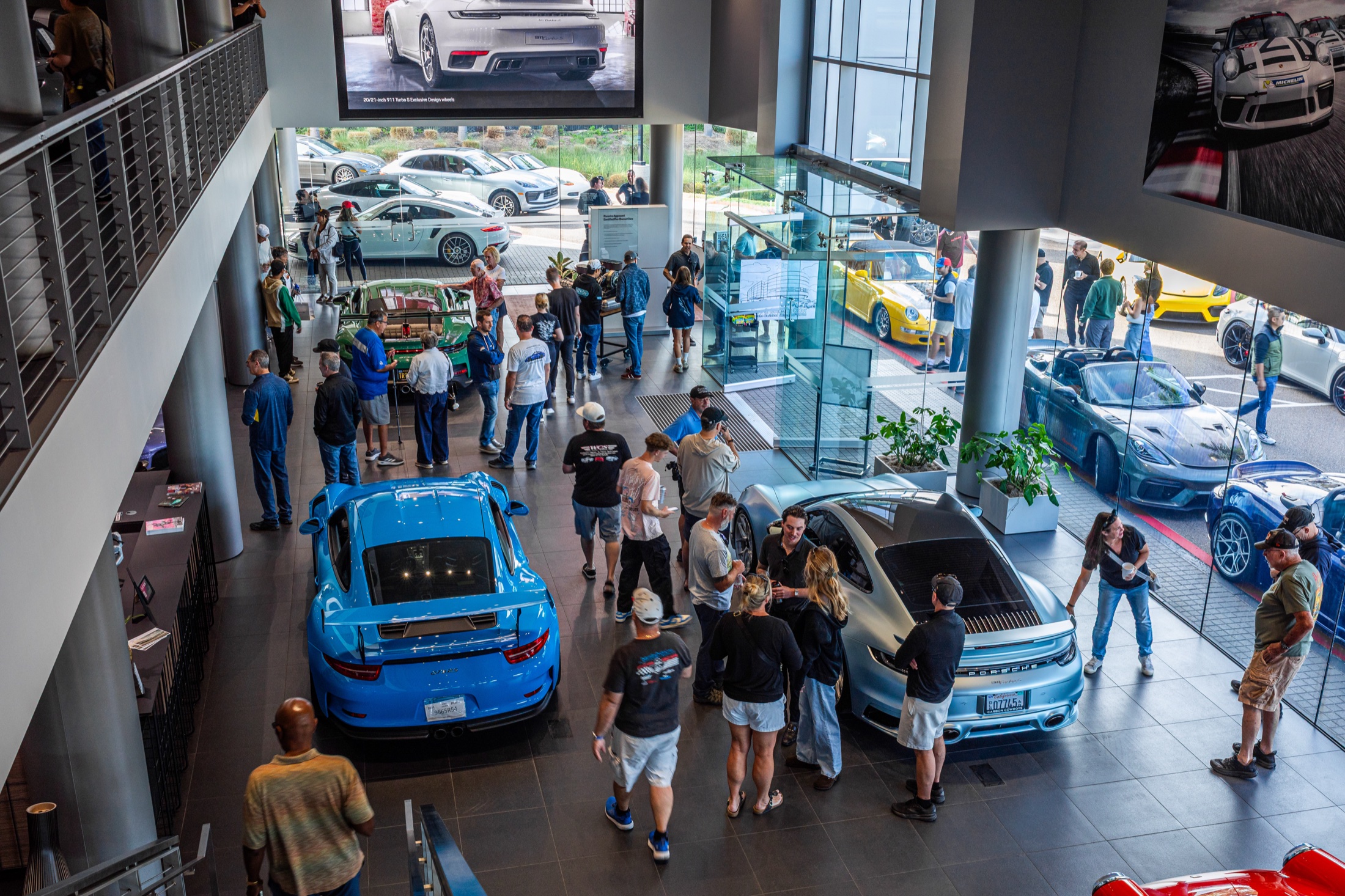 Brightly colored Porsches surrounded by visitors in the showroom at Cars and Coffee In Color