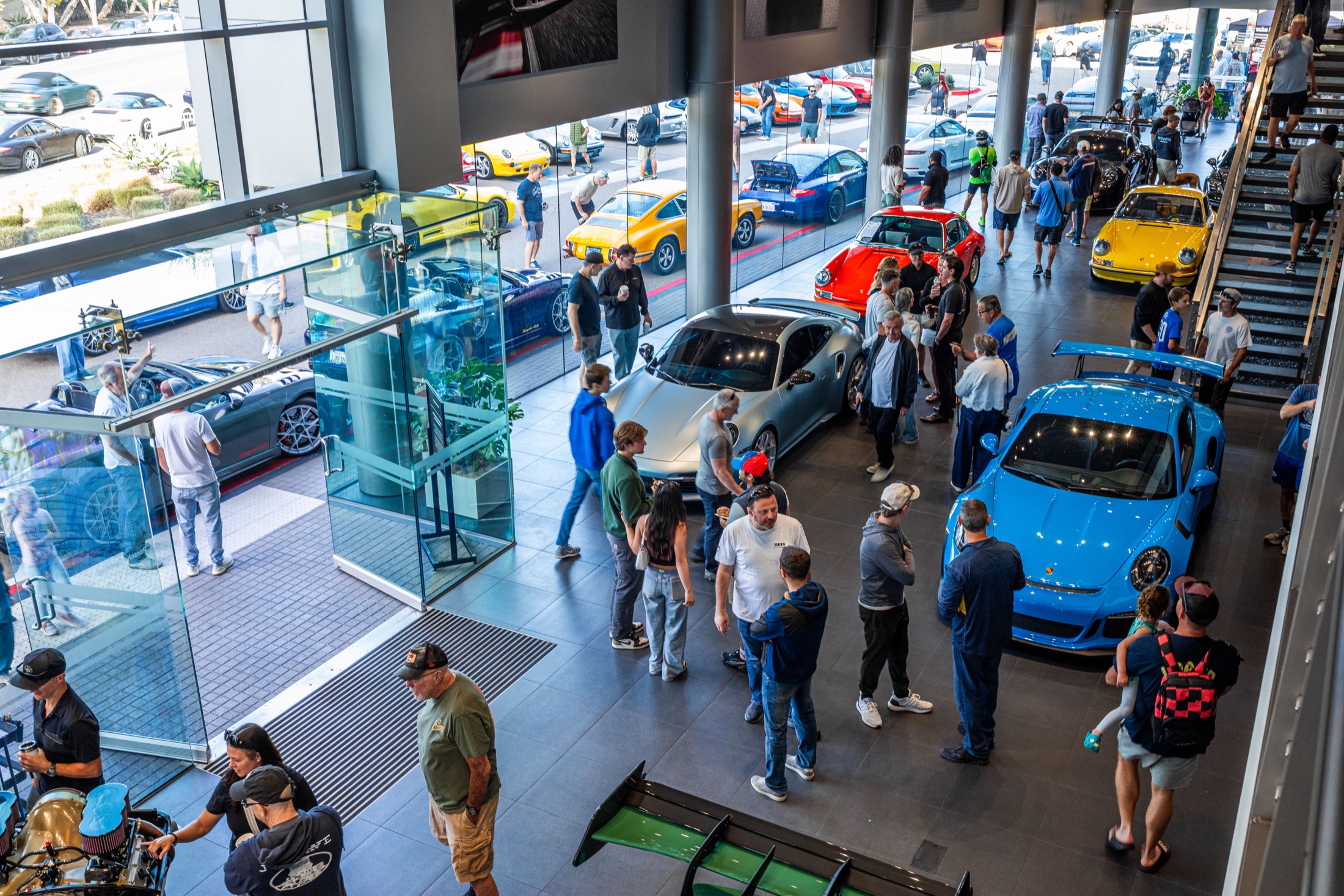 View across the showroom full of colorful Porsches and visitors at Cars and Coffee In Color