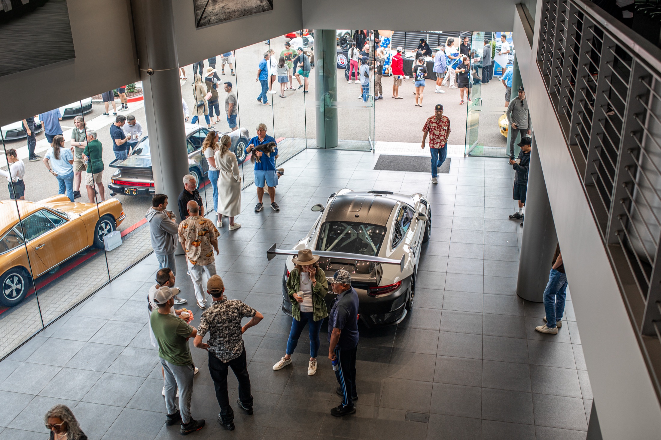 Visitors watching a car roll through the Porsche Carlsbad showroom during the anniversary Cars and Coffee