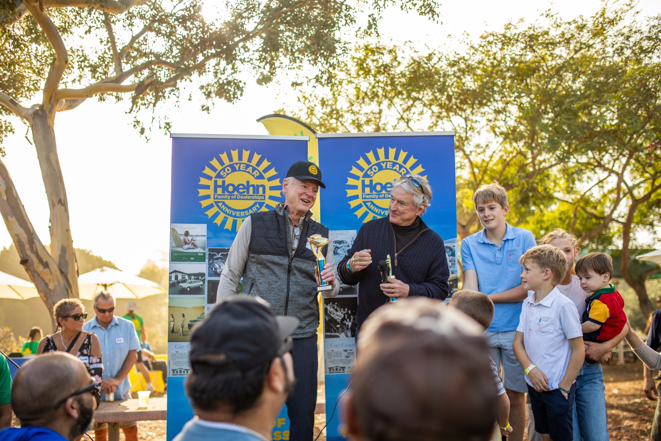Speakers at the Hoehn 50th anniversary banner surrounded by employees and their families at the company picnic