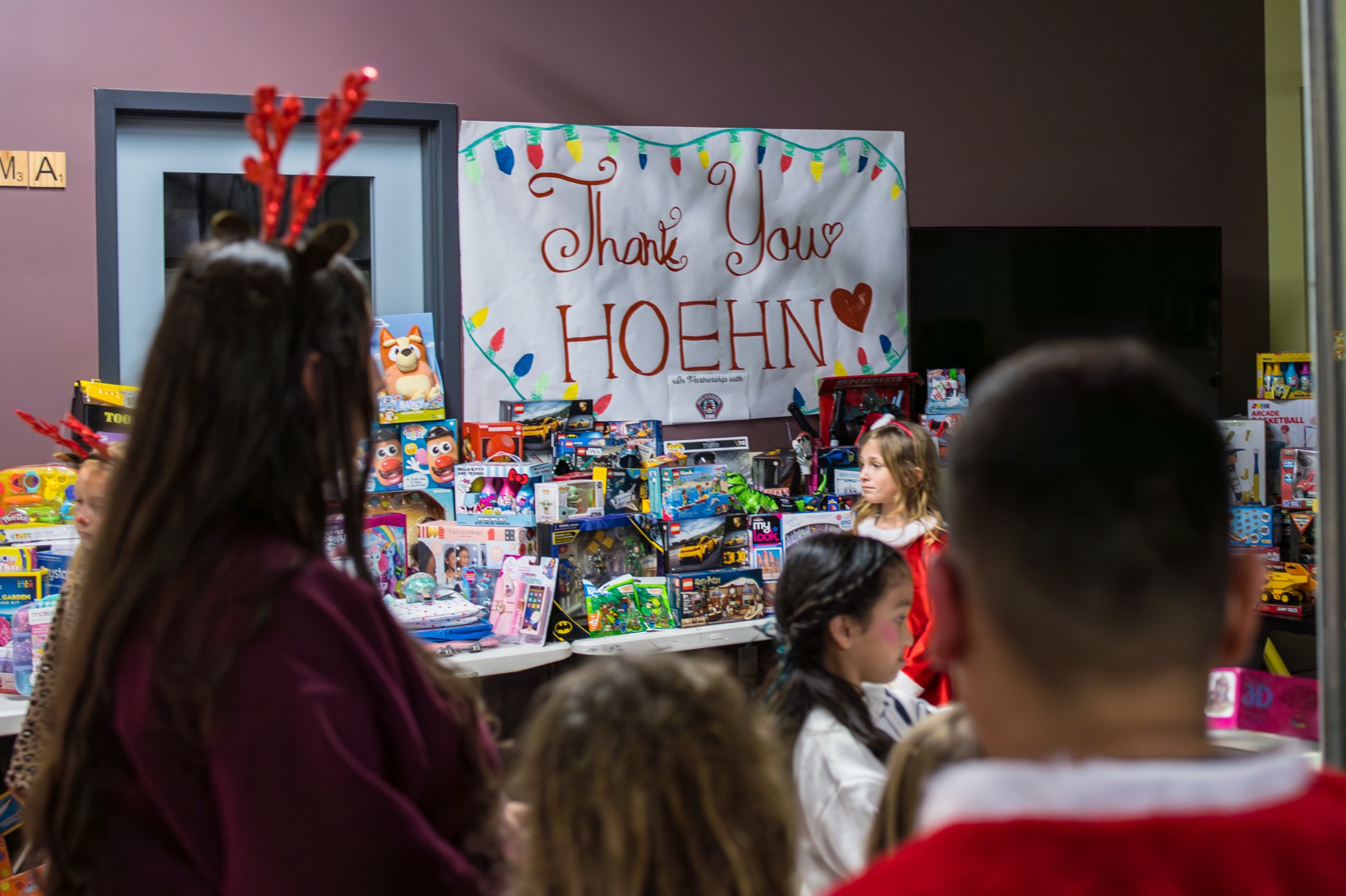 Children at tables full of donated toys beside a Thank You Hoehn sign at the Boys and Girls Club